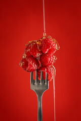 Sweet ripe fresh raw raspberries  edible fruit on silver colour fork with pouring honey or syrup against bright red background full of dietary fiber and vitamins for vegetarian healthy dieting