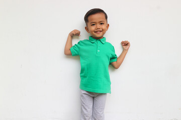A smiling and confidence toddler boy looks at the camera raising his hands isolated on white background