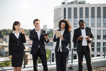 Group of young professionals taking short coffee break and enjoying hot beverage on fresh air. Multiracial coworkers having rest and discussing some working points concerning new business project.