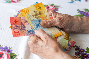 An old woman holds Swiss francs in her hands, banknotes of lower denomination, Pensioners finance concept - obrazy, fototapety, plakaty