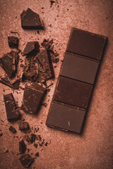 chocolate bar , for the manufacture of confectionery, broken, crumbled, on a brown background, top view,