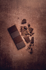 chocolate bar , for the manufacture of confectionery, broken, crumbled, on a brown background, top view,