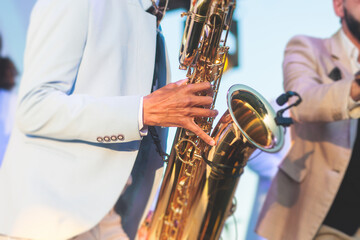 Concert view of saxophonist in a blue and white suit, a saxophone sax player with vocalist and musical band during jazz orchestra show performing music on stage in the scene lights - obrazy, fototapety, plakaty
