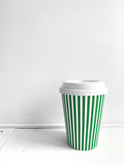 Green striped coffee cup, vertical photo. Street food coffee to go, closed plastic cup for various drinks and beverages on white background. Single object, take away