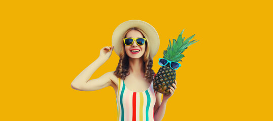 Summer portrait of happy smiling woman with pineapple wearing sunglasses, straw hat posing on yellow background