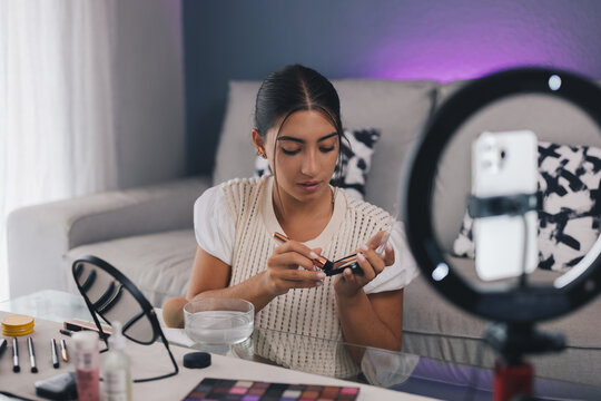Focused female blogger shooting beauty video while doing makeup
