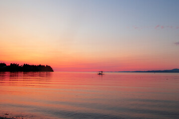 Ocean beach in sunrise and silhouette of a man on paddle boat.