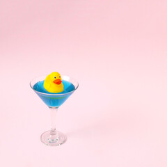 Yellow duck in a martini glass as a swimming pool on a blue background. Creative idea.