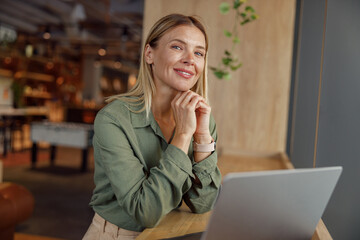 Attractive businesswoman working on laptop in cozy coworking and looking at camera