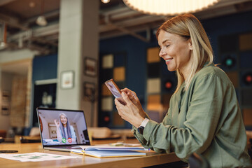 Smiling business woman is using phone during video conference in coworking. Distance work concept