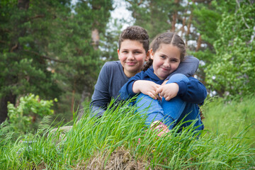 Naklejka na ściany i meble In summer, a brother and sister sit on the grass in the forest.