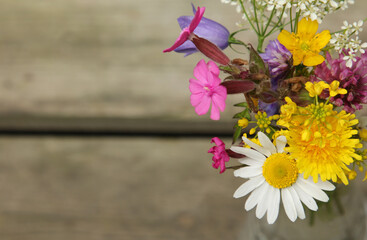 Wildflowers from Finland in a glass bottle on wooden background and space for text. 