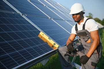 African american man in safety helmet and glasses tighten nuts on solar panels with screwdriver. Competent technician using tools while performing service work on station