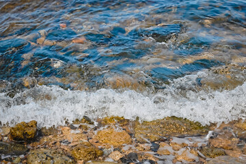 A small wave rolls on the seashore. Multi-colored stones underwater. Background.
