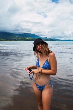 Smiling woman standing on seashore with retro camera