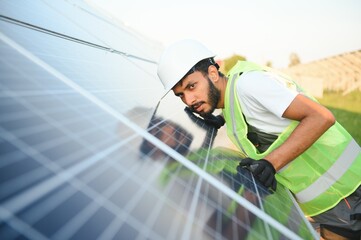 Fototapeta na wymiar Male arabian engineer in helmet and brown overalls checking resistance in solar panels outdoors. Indian man working on station.