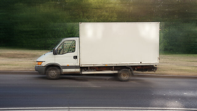 Small cargo truck with empty white side for mock up moving fast on highway. Commercial lorry vehicle with blank banner for advertising information.