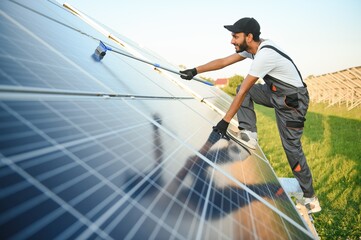 Indian handyman cleaning solar panels form dust and dirt.