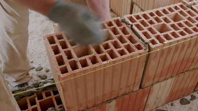 Close-up image of a craftsman on a construction site carefully and responsibly laying red brick. Construction site worker building exterior walls from quality red brick. quality building products