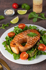 Baked salmon steak served with arugula and cherry tomatoes on a white plate