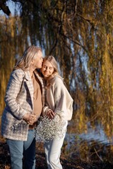 Fototapeta premium Adult daughter hugs her pregnant mom while standing in autumn park