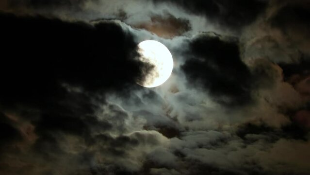 Moon in the blue clouds of the night sky. Clouds fly in front of the full moon. Mysterious Halloween Night