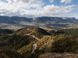 Naklejka premium Landscape of the winding road of the port of Barrerilla with the city of Orduña deep in the valley of Arrastaria and the Gorobel mountain range behind.