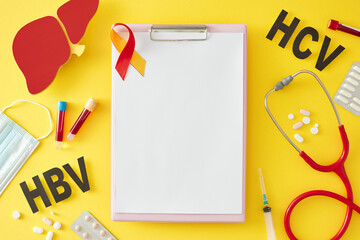 World Hepatitis Day concept. Top view shot of blank clipboard, liver, pills, stethoscope, medical mask, HBV, HCV abbreviation, awareness ribbon, blood samples and syringe on yellow background