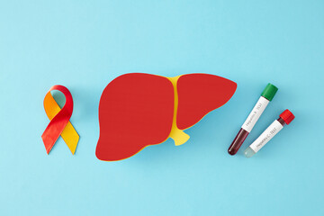 Medical care on World Hepatitis Day. Top view shot of paper liver symbol, awareness ribbon, blood sample on pastel blue background