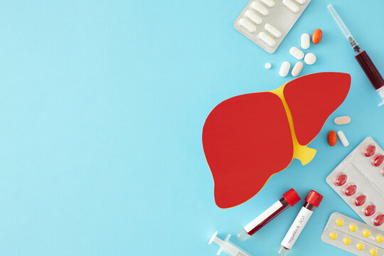 World hepatitis day concept. Top view shot of different pills, liver shape symbol , blood samples and syringes on light blue background with empty space for text