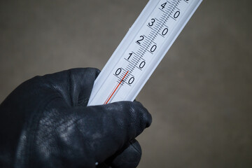 a man's gloved hand holds a thermometer with a low plus temperature in room.