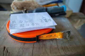 a construction tape measure on which there is a piece of paper with measurement figures, a wooden desktop background