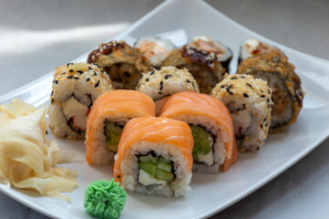 On a white plate there is a set of rolls with salmon, sesame seeds and tempura