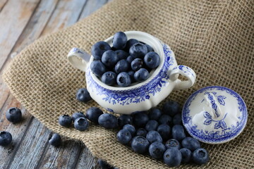 Bowl of fresh blueberries on on a piece of jute, Close up. European blueberry in a blau bowl on jute fabric and wooden table. 