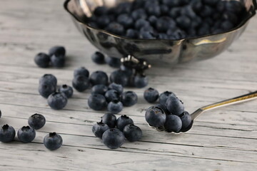 Blueberries in a silver bowl and a silver spoon on a wooden table