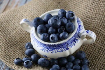 Bowl of fresh blueberries on on a piece of jute, Close up. European blueberry in a blau bowl on jute fabric and wooden table. 