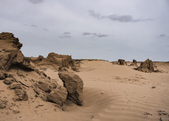 Landscape in the desert with sandy remnants and sandstone in cloudy weather, sand texture in the foreground