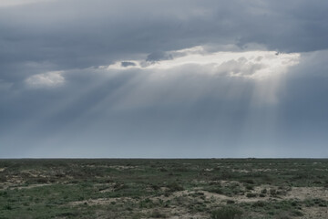 Through a dense layer of clouds and clouds, the sun's rays break through in the desert steppe, in cloudy weather.