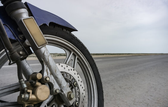 Motorcycle wheel on the background of an asphalt road in the Kazakh steppe, in cloudy weather in the desert