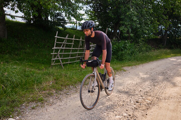 Fototapeta premium Gravel biking. Male cyclist riding downhill by a gravel road. Man is cycling in the nature.