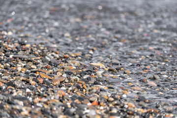 Colored pebbles on the beach of Greece with the waves of the sea covering them during a sunny day.