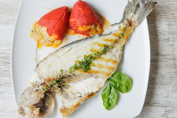 Grilled gilt-head bream on a white plate accompanied by stuffed piquillo peppers