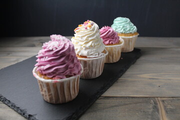 Three four cupcake cakes with a cream cap of white green lilac color on a black dark background with space for text