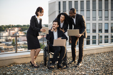 Group of international professionals together with disabled man meeting in open air on roof and analyzing new project via modern technologies. Short haired lady demonstrating data on digital tablet.