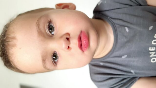 Beautiful Caucasian toddler boy wearing grey t-shirt looking at camera. Close up portrait of a cute peaceful baby. Vertical screen.