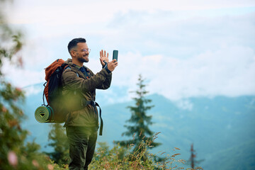 Happy hiker making video call via smart phone in mountains.