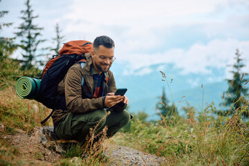 Happy backpacker texting on cell phone while hiking in mountains.