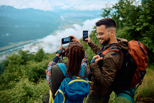 Happy couple of backpackers taking pictures with smart phones while hiking in mountains.
