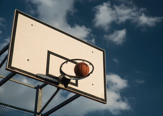 Piłka do koszykówki wpadająca do kosza, na tle błękitnego, słonecznego nieba. - obrazy, fototapety, plakaty