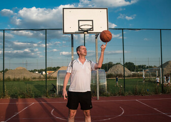 Mężczyzna kręcący piłkę do koszykówki na palcu na boisku na świeżym powietrzu, w słoneczny dzień. - obrazy, fototapety, plakaty